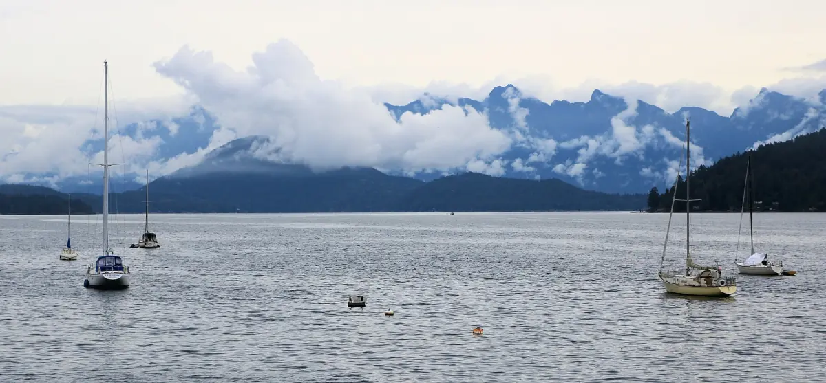 Sailboats at anchor off Gibsons with snowy coast mountains in the distance