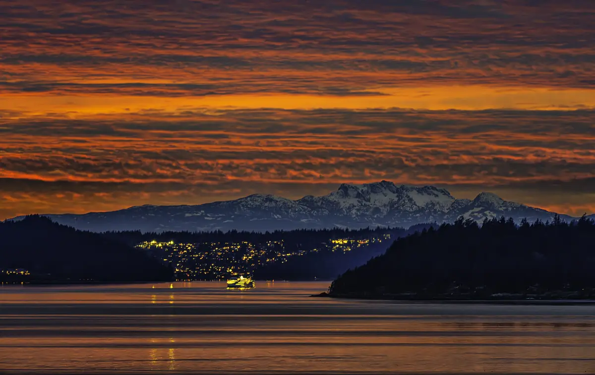 Orange evening sky over Howe Sound with distant lights and mountains
