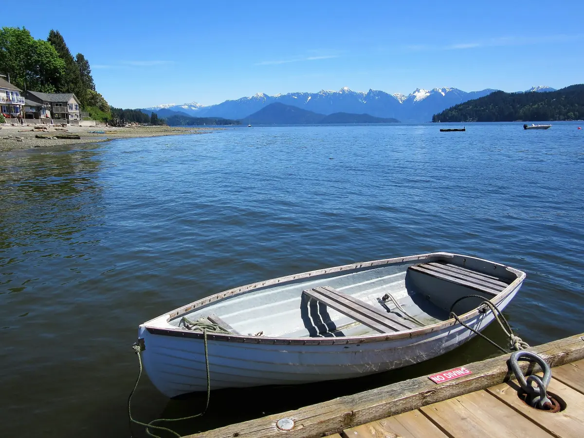 Small white rowboat moored at a dock with snowy mountains across the sound