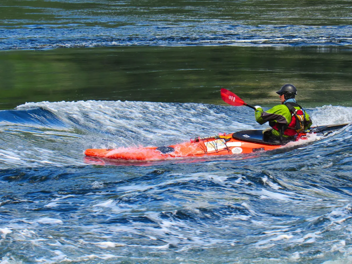 Kayaker paddling an orange kayak through a standing wave at Skookumchuck