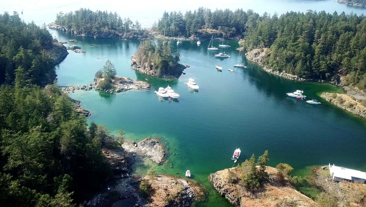 Aerial view of turquoise inlet with boats and forested islets at Smuggler Cove