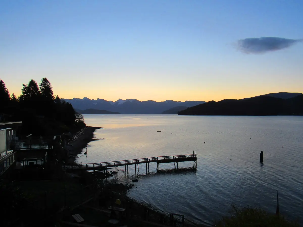 Dusk over a still inlet with a wooden dock and distant mountains
